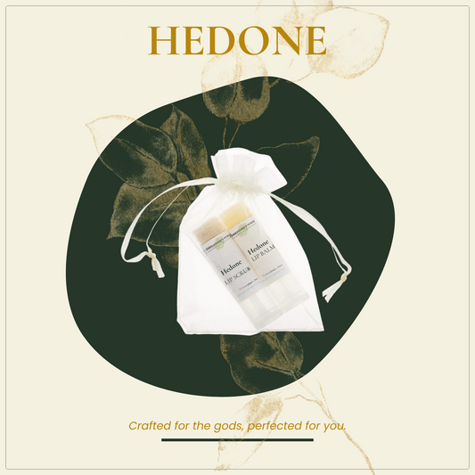 A package of Hedone lip balm and scrub duo, with a white and clear packaging tied with a ribbon and green leaves around it. The text on the packaging reads 'Hedone' and 'Crafted for the Gods, Perfected for You.